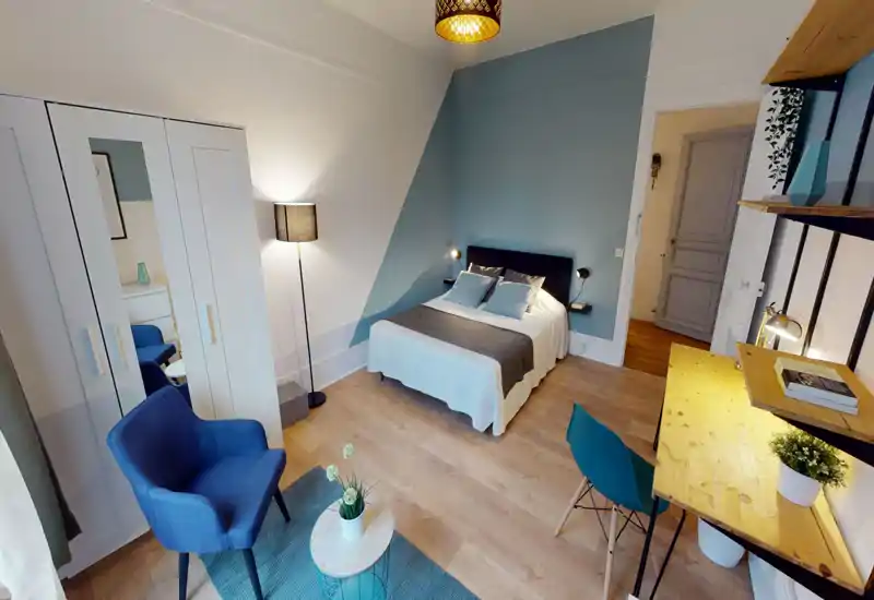 Sunny, stylish bedroom with a double bed against a blue-accent wall, cozy textiles and a small workspace — ideal for comfortable stays.