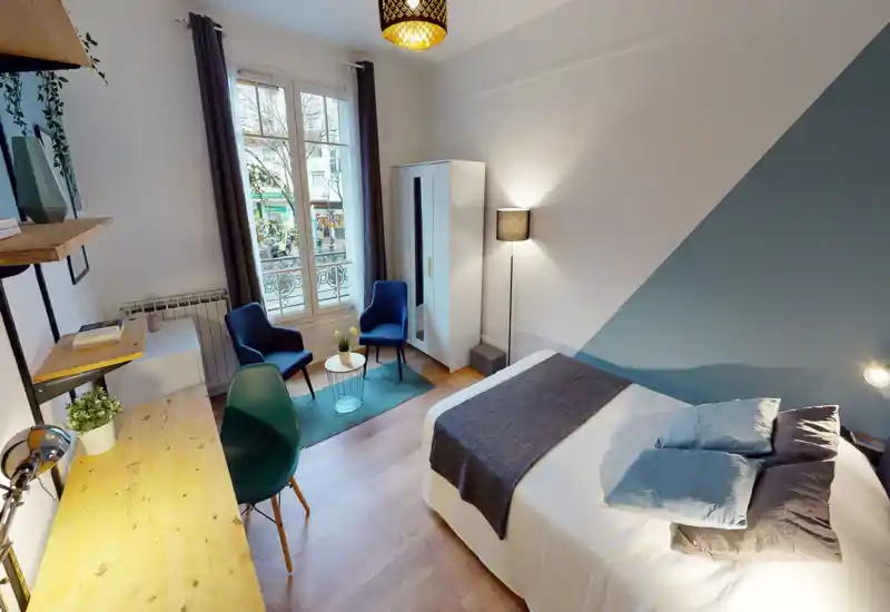Bright, well-staged bedroom with a double bed, bedside lighting and a seating corner by the window — ideal for rentals seeking a modern, cozy feel.