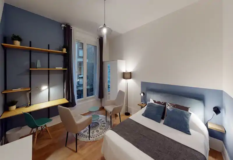 Bright, styled bedroom with a comfortable double bed, bedside lamps, and a small seating area by the window. Wooden floor, coordinated cushions and headboard give a cozy, modern feel — ideal for rental photos.