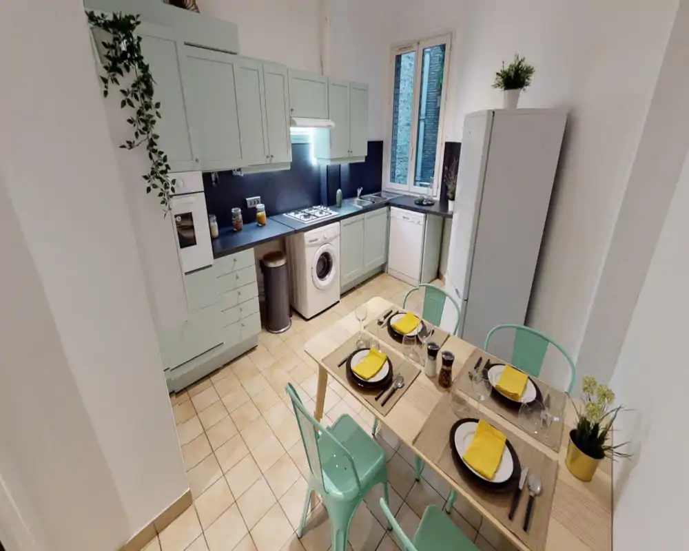 Well-appointed kitchen with pastel cabinets, integrated appliances, a washing machine and a small dining table set for four — bright, tidy and stylishly staged.