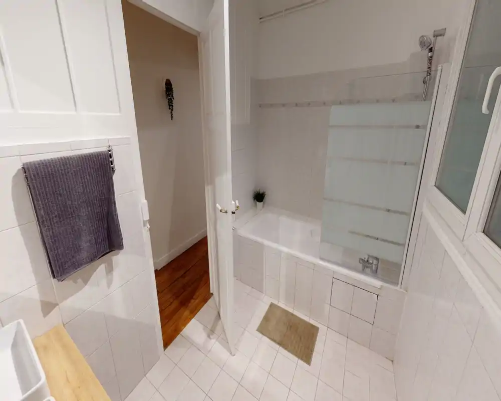 Clean, bright bathroom with a tiled bathtub and glass shower screen, white tiles and a small plant for a fresh touch.