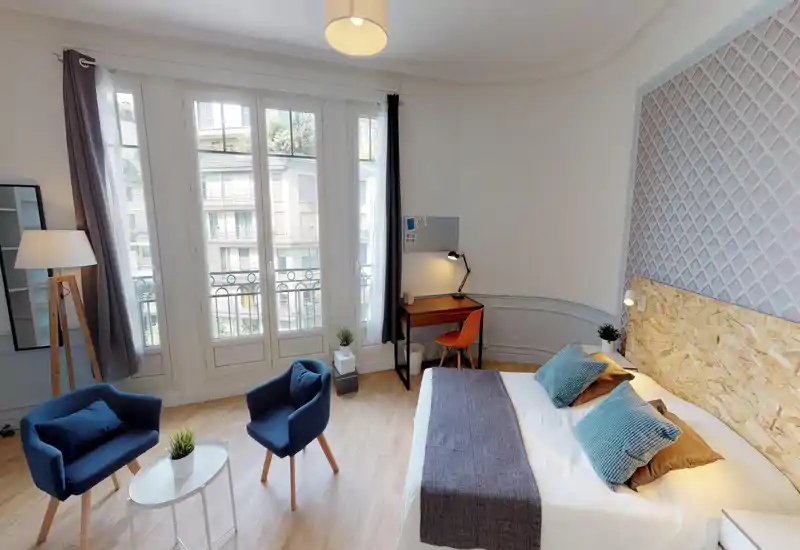 Camera da letto luminosa e di stile con ampie finestre alla francese, letto matrimoniale con testiera e cuscini decorativi, area salotto e scrivania — perfetta per soggiorni confortevoli.