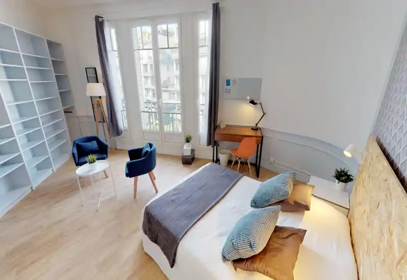 Camera da letto luminosa e moderna con un grande letto matrimoniale, cuscini e plaid accoglienti e luce naturale da ampie finestre; presente anche un angolo studio e zona con sedute.