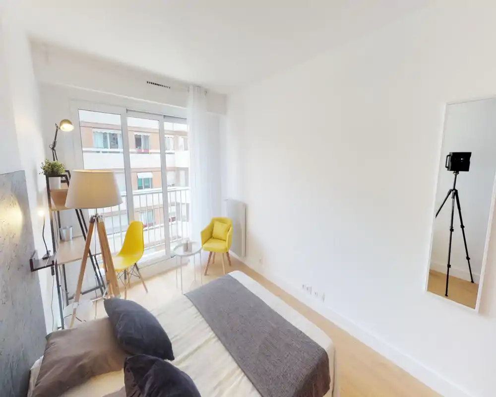 Bright, modern bedroom with a neatly made double bed, soft textiles and two yellow accent chairs by a large window offering natural light.