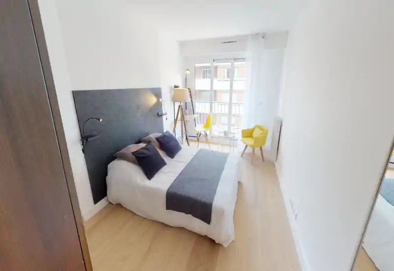 Bright, modern bedroom with a double bed framed by a dark headboard, soft textiles and natural light from a balcony window — ideal for rental photos.