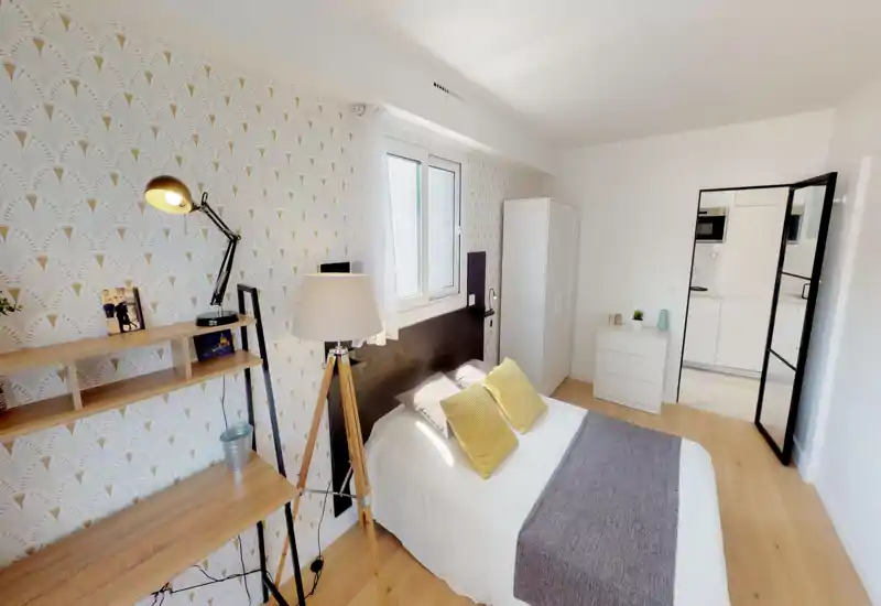 Camera da letto luminosa e ben arredata con letto matrimoniale, cuscini decorativi e carta da parati coordinata; luce naturale dalla finestra e lampade calde offrono un’atmosfera accogliente.