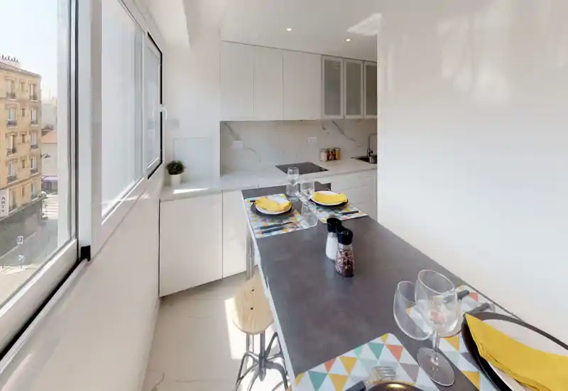 Cucina moderna e luminosa con penisola per la colazione; mobili bianchi, paraschizzi effetto marmo e grande finestra che assicurano molta luce naturale.