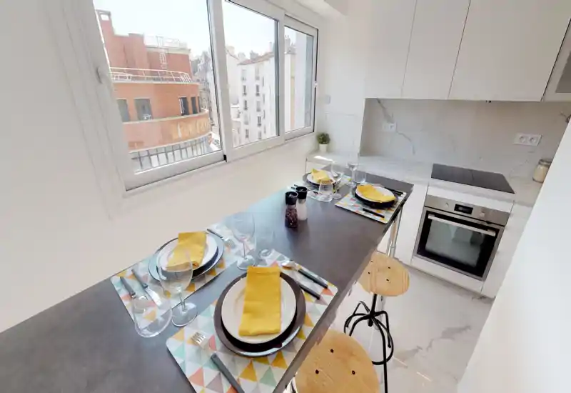 Bright, modern open kitchen with a breakfast bar set for four, marble-effect counters, integrated oven and large windows providing city views.