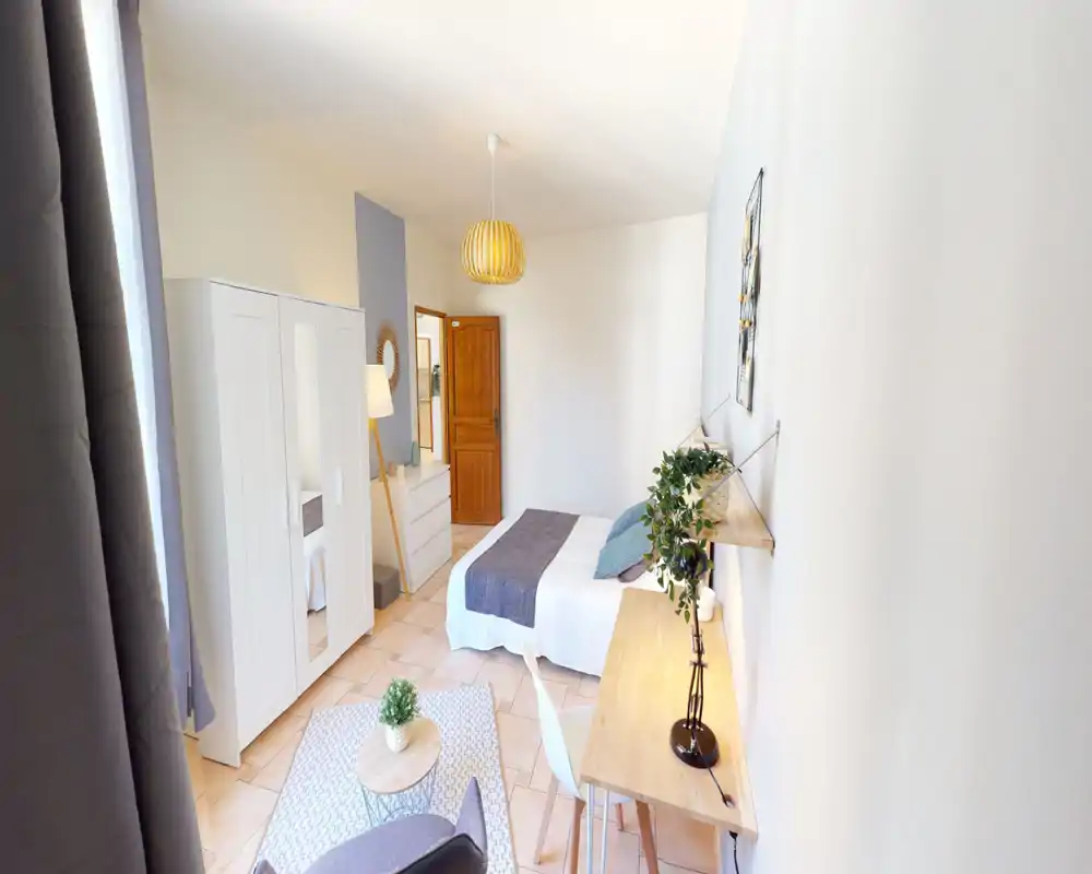 Bright, neatly staged bedroom with a double bed dressed in neutral linens, a wardrobe and a small desk. Natural light and soft decor create a welcoming atmosphere ideal for rental listings.