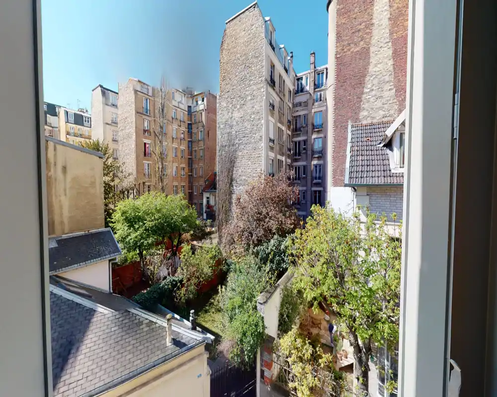 Sunny view over a leafy courtyard garden framed by neighboring apartment buildings — ideal to highlight a quiet urban green space and natural light.