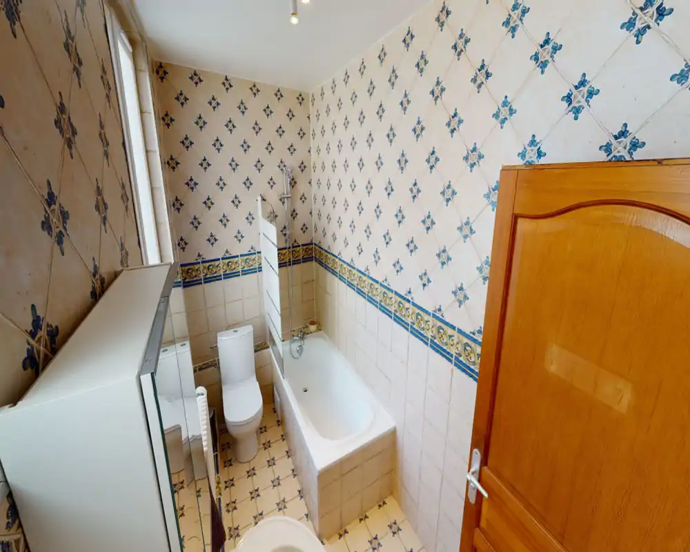 Tidy bathroom with a bathtub and toilet, classic patterned tiles and a mirrored cabinet. Bright, well-lit space suitable for rental listings.