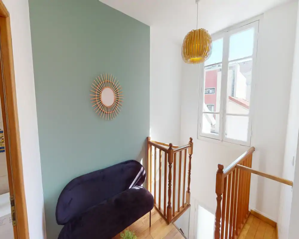 Small, bright landing/entrance area with decorative mint-green accent wall, a compact velvet bench, wooden stair railing and a pendant light—ideal as a welcoming upstairs landing or reading nook.