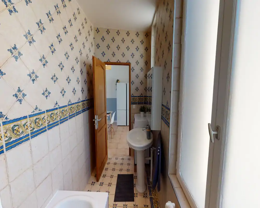 Well-lit bathroom with classic decorative tiles, a pedestal sink and a window providing natural light.