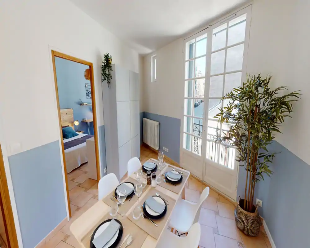 Bright, well-styled dining area with a set table for six, white chairs and natural light from large French doors opening to a small balcony.