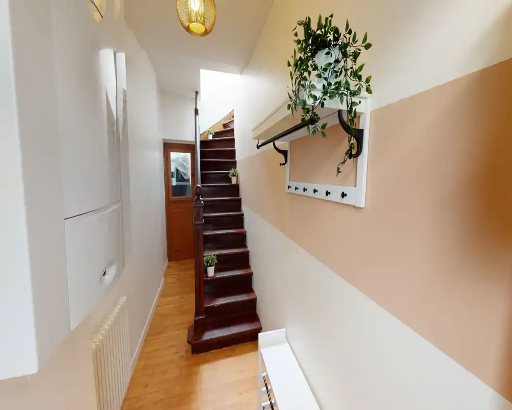 Bright, narrow entrance hallway with wooden stairs, wall hooks and decorative plants — ideal first impression for a cozy home.