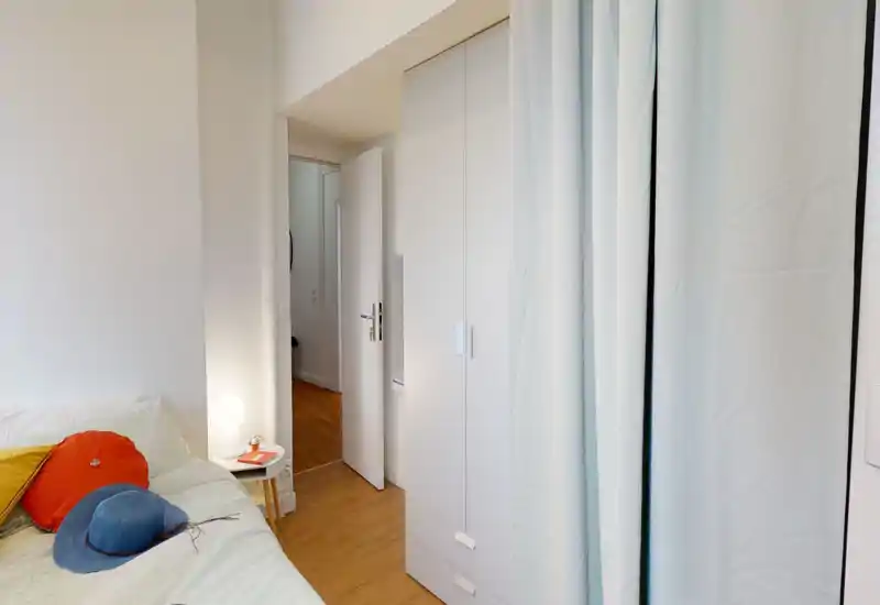 Angolo camera ben illuminato con letto ordinato, cuscini colorati e comodino con lampada — luminoso, accogliente e dall’arredamento semplice.