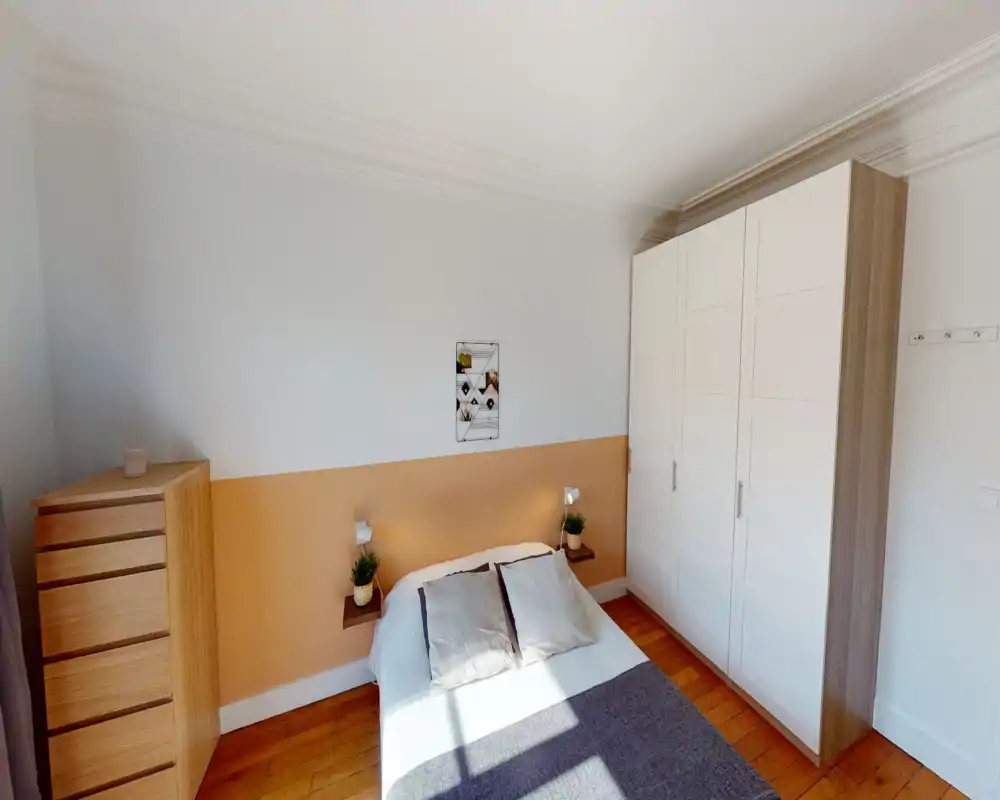 Sunny, neatly styled bedroom with a double bed, warm accent wall and built-in wardrobe. The room features wooden floors, bedside shelves with plants and ample natural light.