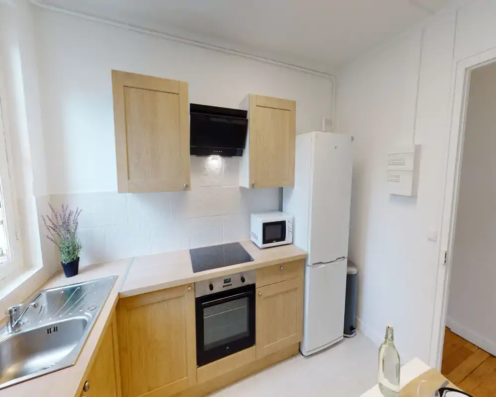 Bright modern kitchen with wooden cabinets, built-in oven and induction hob, refrigerator and microwave, plus a sink area by the window — a clean, practical cooking space.