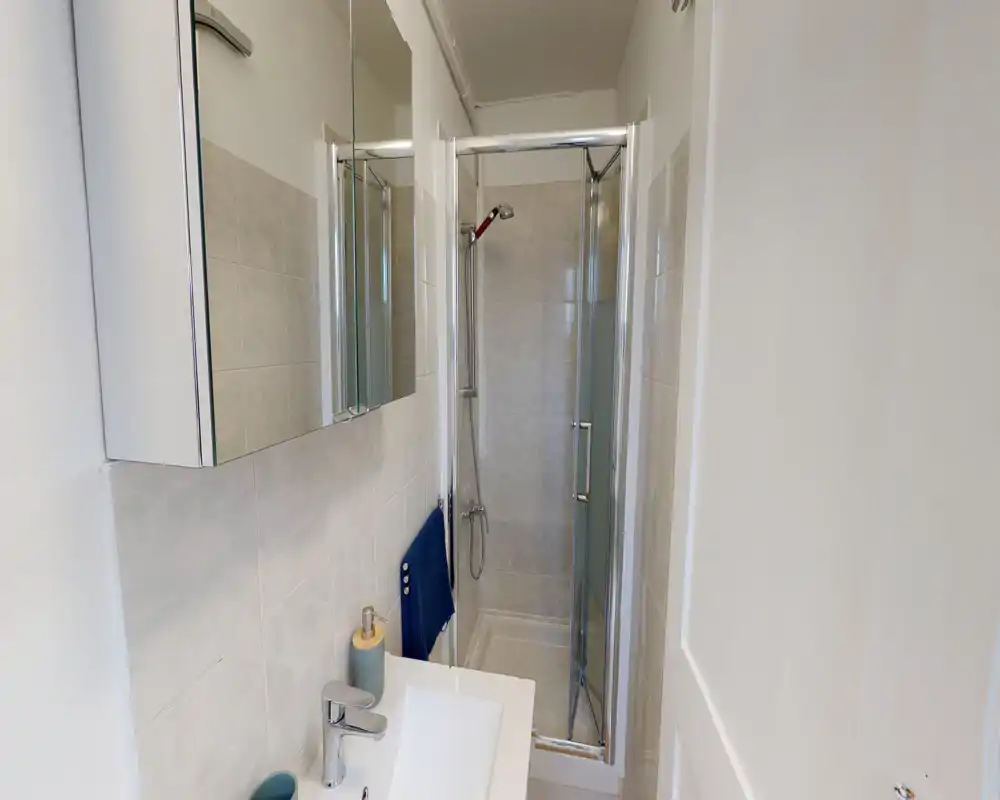 Compact, modern bathroom with a tiled shower cubicle, wall-mounted mirror cabinet and a washbasin with chrome fixtures. Bright neutral tiles and simple accessories create a clean, functional space ideal for short stays.