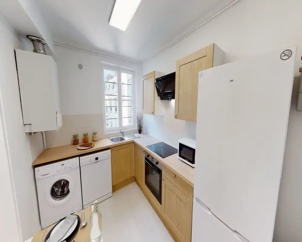Bright, compact kitchen with wooden cabinets, built-in oven and induction hob, fridge, dishwasher and washing machine; neat countertop and window providing natural light.