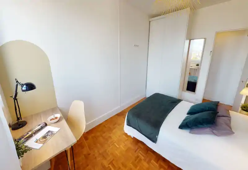 Chambre lumineuse et soignée avec lit double habillé de linge coordonné, parquet et petit bureau près de la fenêtre — idéale pour un séjour confortable.