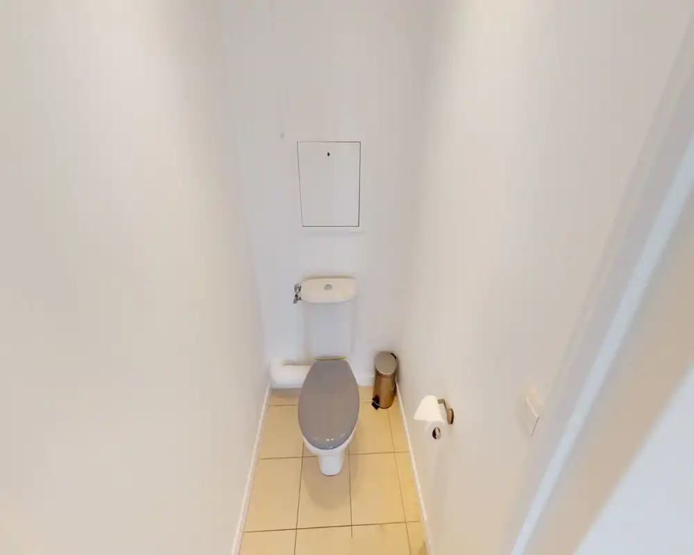 WC compact et propre avec toilette moderne, petite poubelle et sol carrelé dans un espace étroit et bien éclairé.
