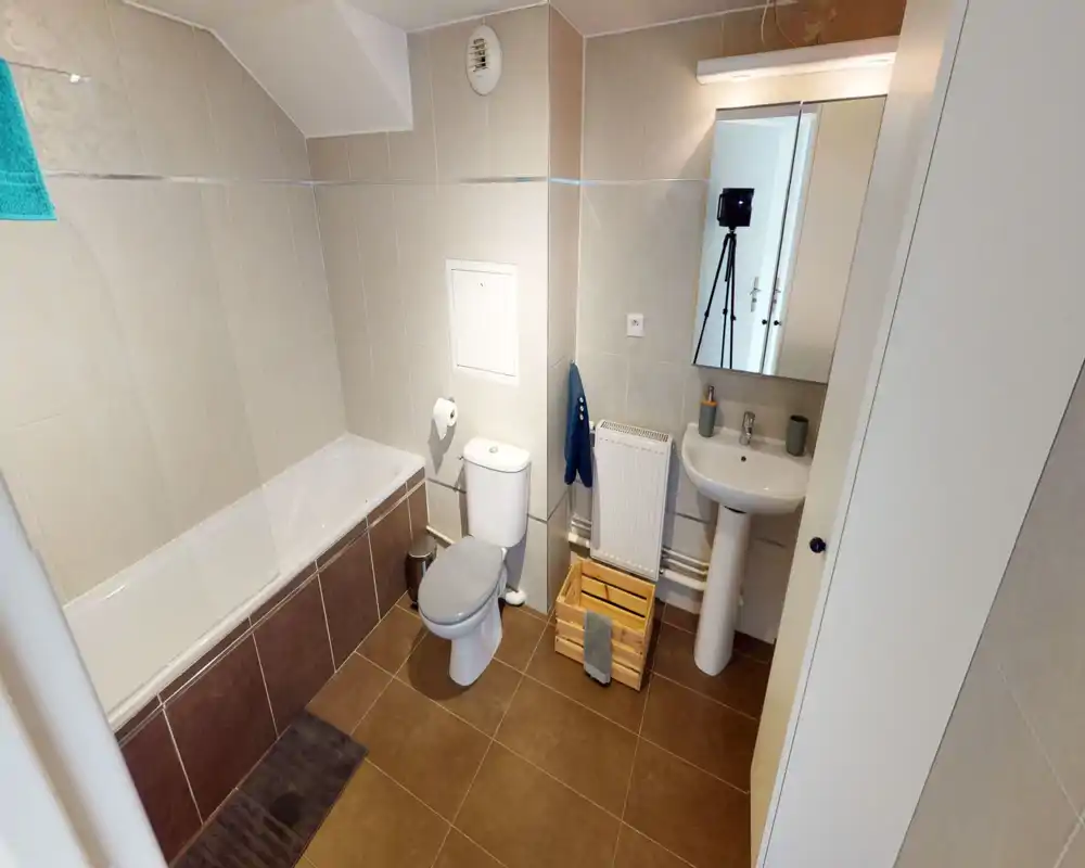 Salle de bains moderne et propre avec baignoire, WC et lavabo sur colonne ; carrelage neutre et sol chaud pour un espace fonctionnel et soigné.