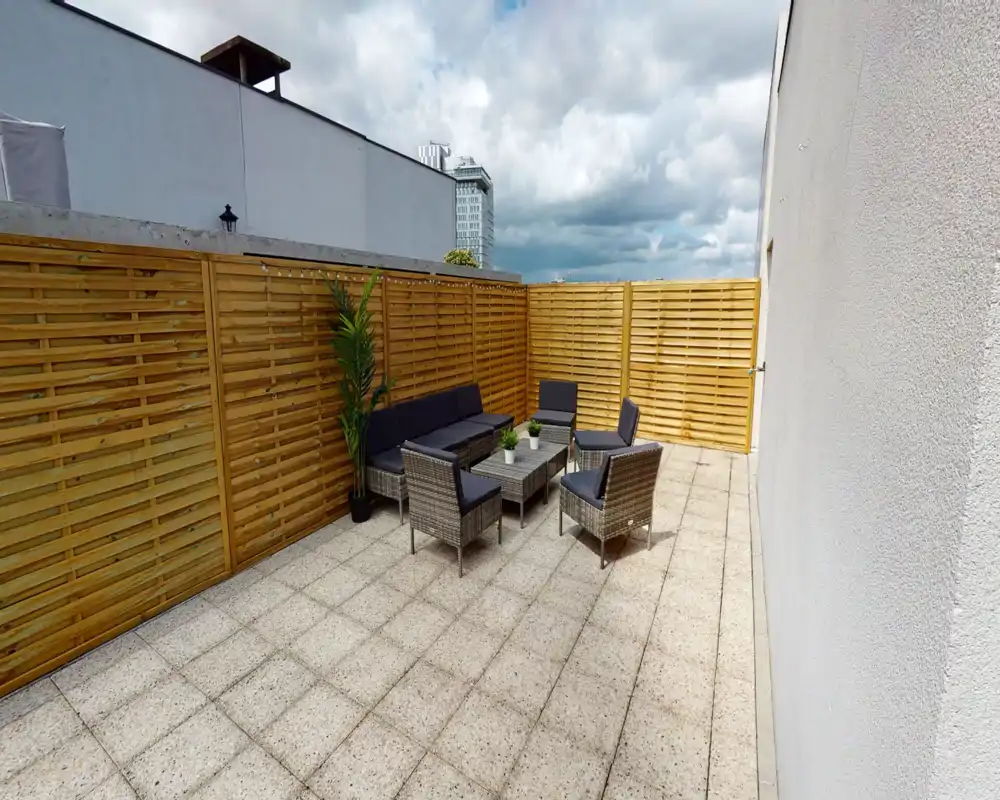 Terrasse privée ensoleillée avec salon en rotin pour six personnes, sol carrelé et panneaux de bois pour l'intimité — idéale pour se détendre à l'extérieur ou pour de petites réunions.