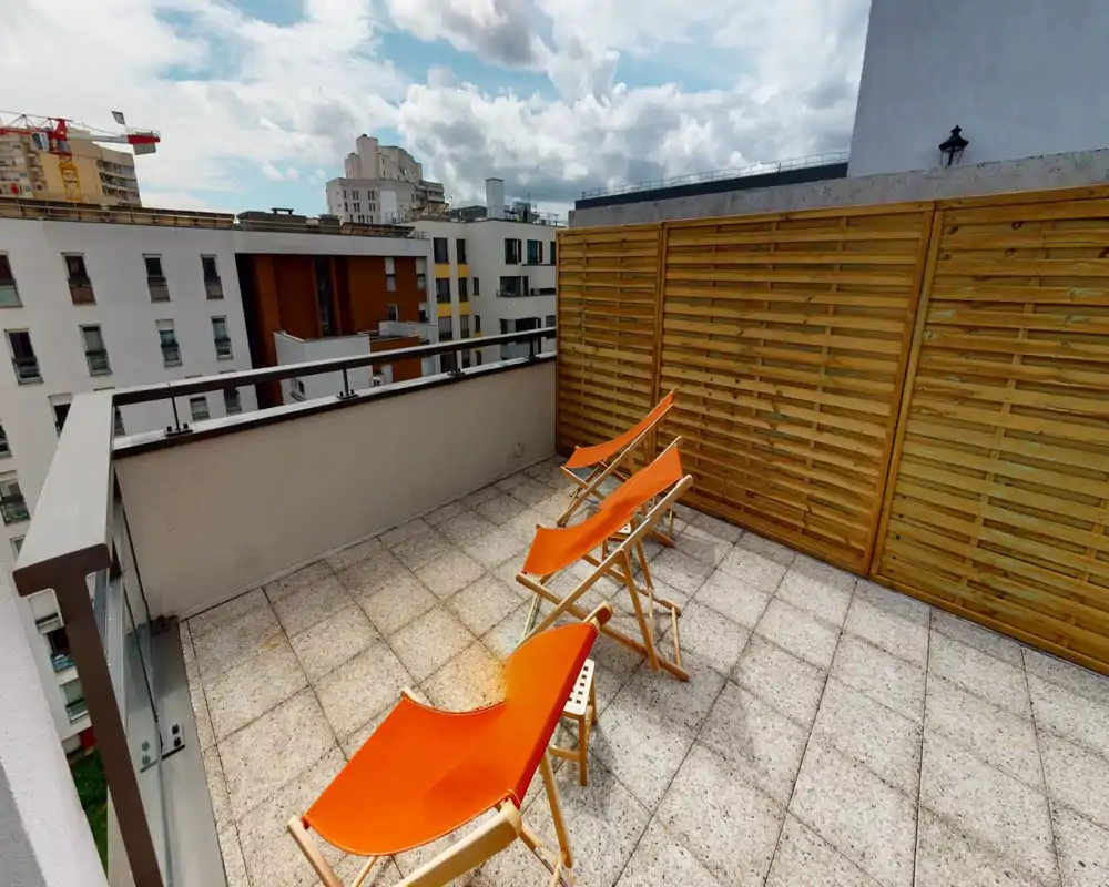 Terrasse privée ensoleillée avec trois bains de soleil orange, sol carrelé et claustra en bois pour l'intimité — idéale pour se détendre en plein air avec vue sur la ville.
