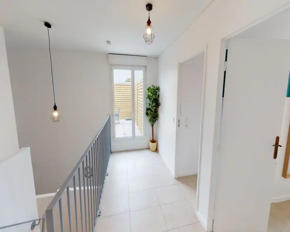 Palier à l'étage lumineux avec garde-corps, sol carrelé et porte vitrée donnant sur une petite terrasse extérieure. Luminaires modernes et plante en pot offrent un espace de transition épuré.
