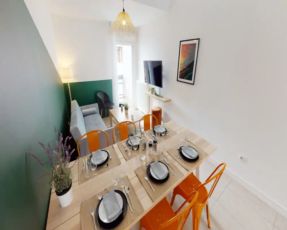 Espace salon-salle à manger lumineux et moderne avec table dressée, chaises orange et un canapé gris confortable près d'une table basse et d'une TV — idéal pour recevoir.