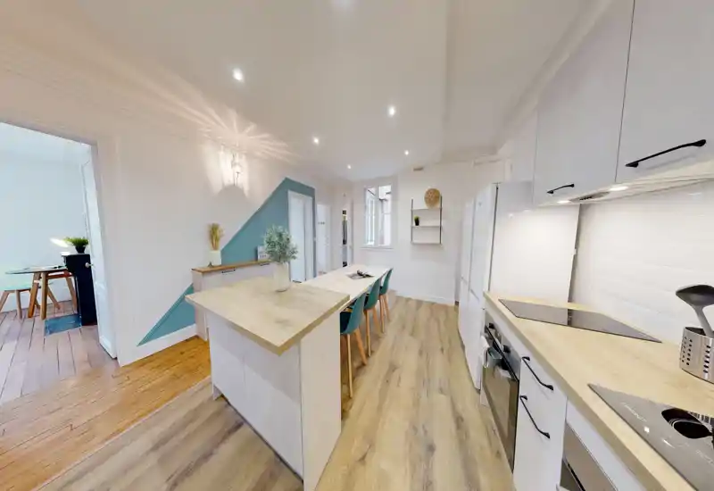 Cucina moderna open space con isola centrale, piani in legno e sgabelli coordinati. Ambiente luminoso e curato con elettrodomestici integrati e pavimento in legno caldo.