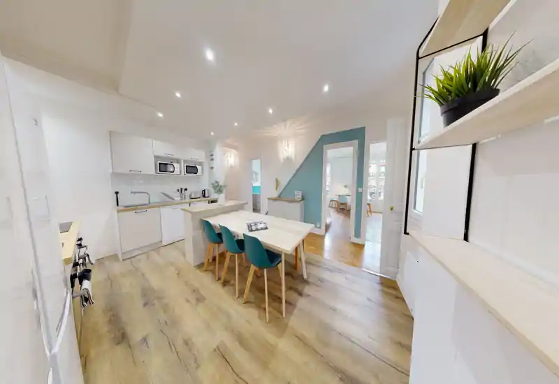Cucina open-space luminosa e moderna con elettrodomestici integrati e isola pranzo con quattro sedie turchesi — pavimento in legno elegante e mobili bianchi puliti creano un ambiente accogliente.
