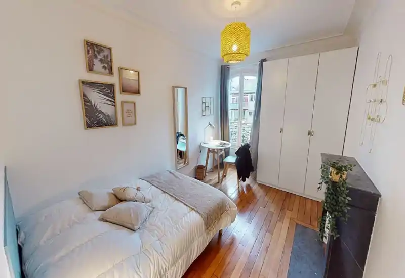 Camera da letto luminosa e accogliente con letto matrimoniale rifatto, pavimenti in legno e armadio. Una piccola scrivania vicino alla finestra e quadri alle pareti completano l’ambiente curato.