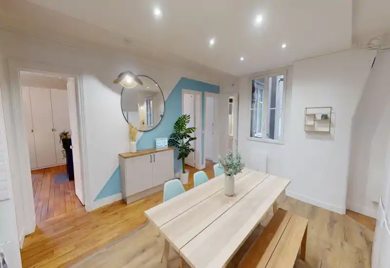 Salle à manger lumineuse et aménagée avec une table en bois clair, banc et chaises pastel. Miroir décoratif, plantes et rangement minimaliste offrent une atmosphère moderne et accueillante.