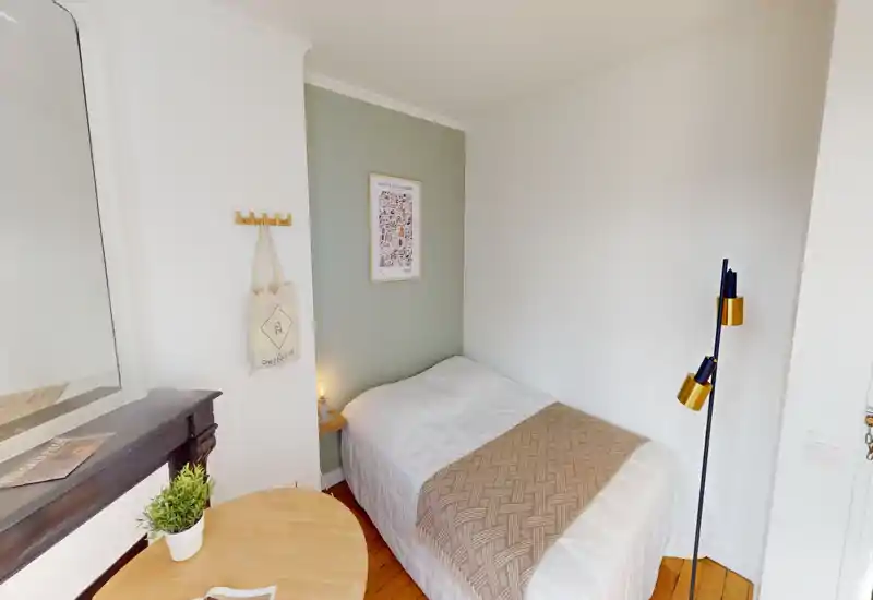 Small, neatly styled single bedroom with a white duvet, woven throw and bedside lamp; light wood floor and soft neutral tones create a cozy feel.