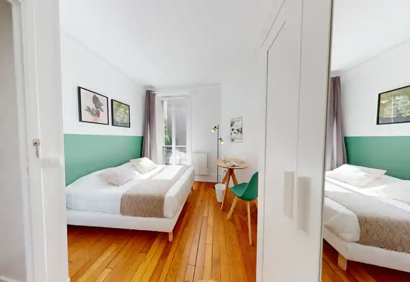 Chambre moderne et lumineuse avec un lit complet, un mur d'accent vert et un parquet chaleureux. La lumière naturelle entre par une grande fenêtre et la garde-robe avec miroir agrandit l'espace.