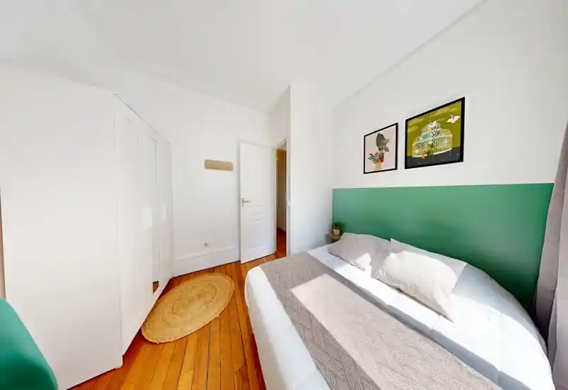 Chambre lumineuse et bien mise en scène avec lit double devant une tête de lit verte, parquet et tableaux encadrés — espace chaleureux et accueillant.