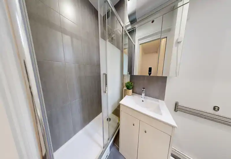 Bagno moderno e compatto con doccia walk-in, parete piastrellata, specchio a armadietto e mobile lavabo bianco — stile contemporaneo e pulito, perfetto per affitti brevi.