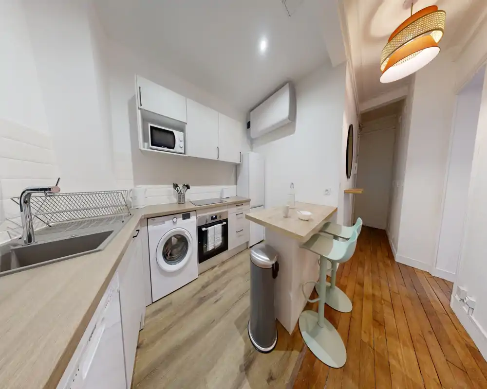 Kitchenette moderne et lumineuse avec appareils encastrés, comptoir petit-déjeuner et sol en bois — idéale pour un studio urbain élégant.