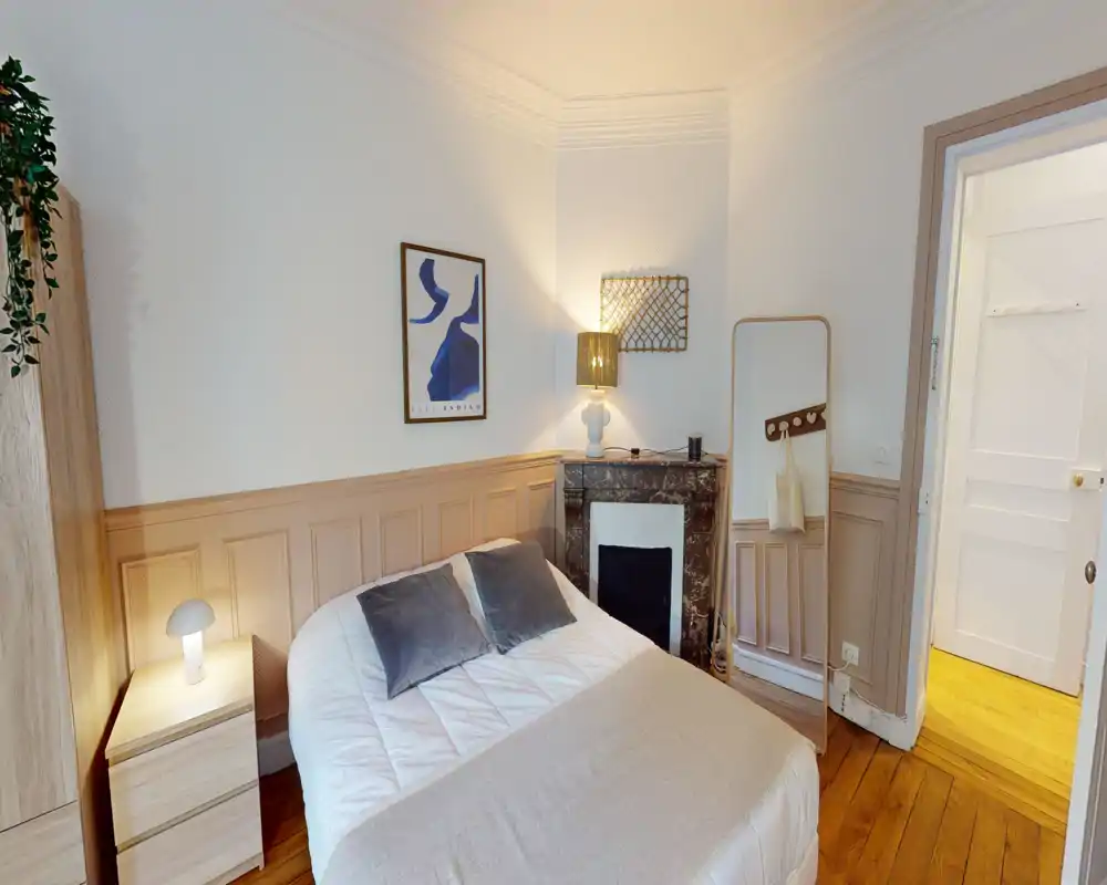 Bright, stylish bedroom with a neatly made double bed, soft linens and decorative cushions; warm bedside lighting and a full-length mirror add charm.