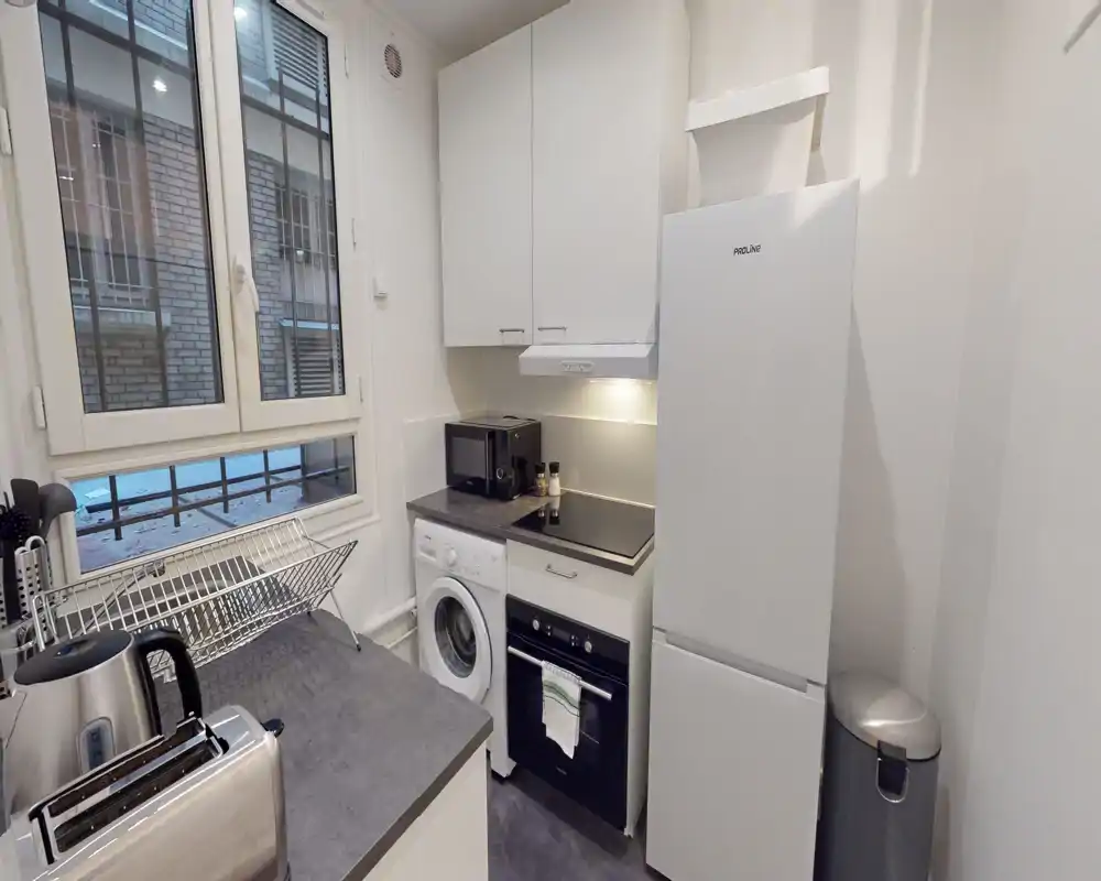 Compact modern kitchen with integrated appliances, including fridge, oven, washing machine and countertop microwave. Bright, efficient layout ideal for a city apartment.