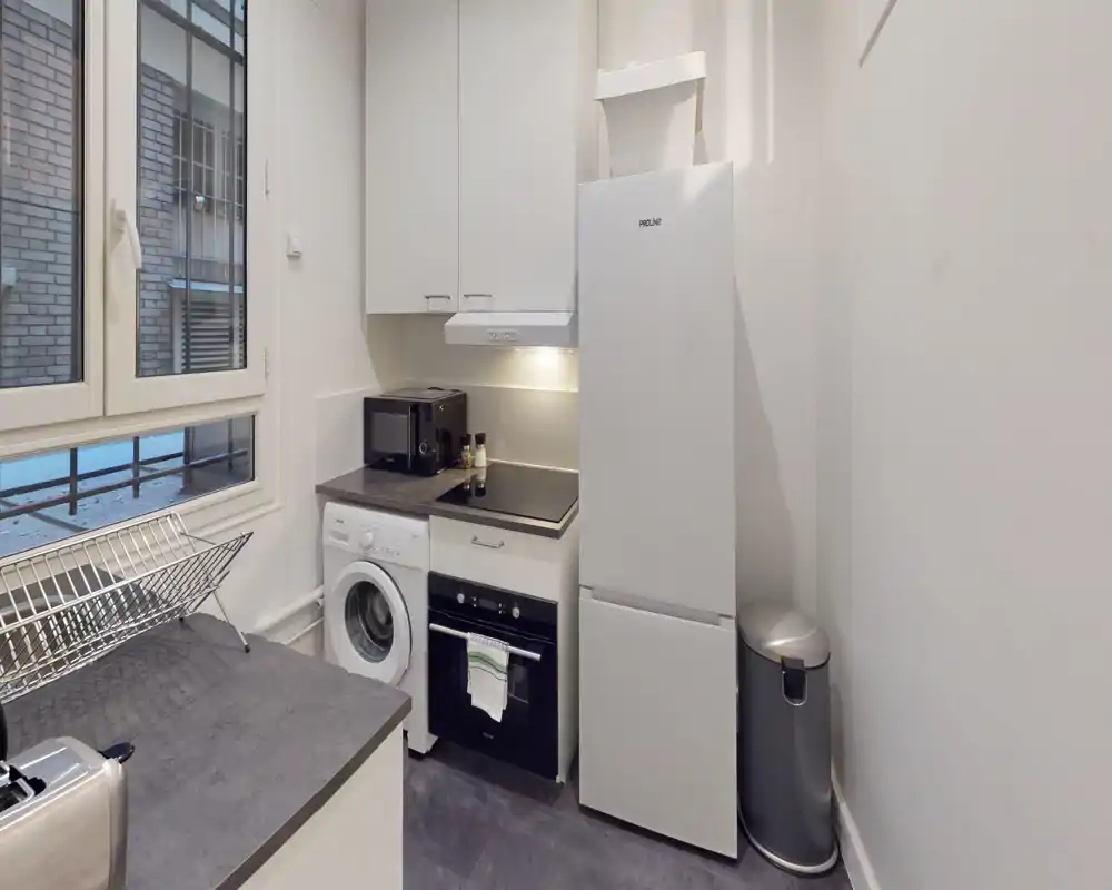 Compact modern kitchen with built-in oven, fridge-freezer and induction hob; a washing machine is integrated under the counter. Bright, efficient layout ideal for a small apartment.