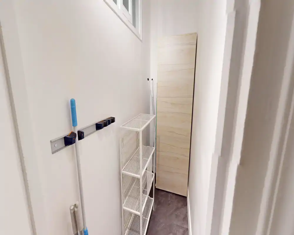 Narrow utility closet with wall-mounted mop holders and a metal shelving unit — ideal for storage and cleaning supplies.