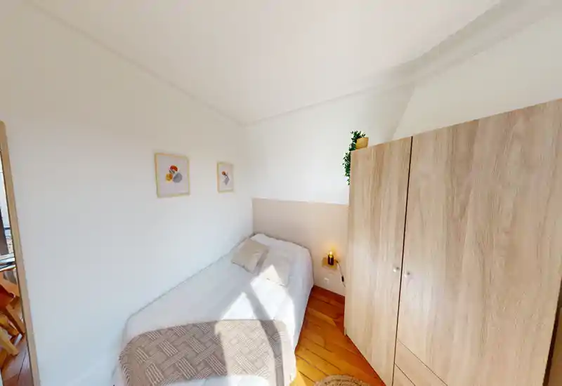 Chambre simple et lumineuse avec un lit bien fait, une armoire en bois et un parquet chaleureux. Tons doux, plaid décoratif et lampe de chevet créent une atmosphère cosy, parfaite pour une annonce locative.