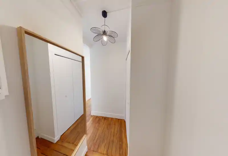 Entrée/couloir étroit avec sol en bois chaleureux, murs blancs et miroir en pied ; un luminaire suspendu décoratif apporte style et luminosité.