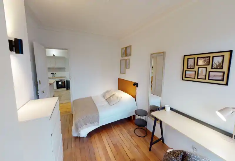 Bright, cozy single bedroom with wooden floors, a neatly made bed, bedside table and a compact desk — ideal for a comfortable stay or a rental listing.