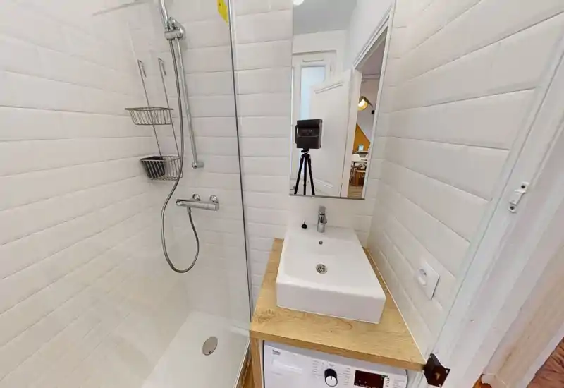 Salle de bain compacte et moderne avec carrelage métro blanc, douche à l'italienne avec cloison en verre, robinetterie murale et vasque rectangulaire sur plan en bois.