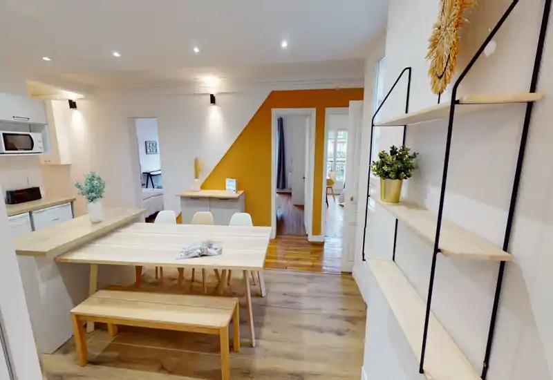 Salle à manger moderne et lumineuse avec table en bois, banc et chaises, mur d'accent moutarde et vue ouverte sur les pièces adjacentes — idéale pour valoriser l'espace commun.