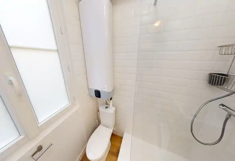 Petite salle de bain moderne avec carrelage métro blanc, douche à l'italienne avec paroi en verre, chauffe-eau mural et toilette. Lumineuse et propre, adaptée aux annonces locatives.